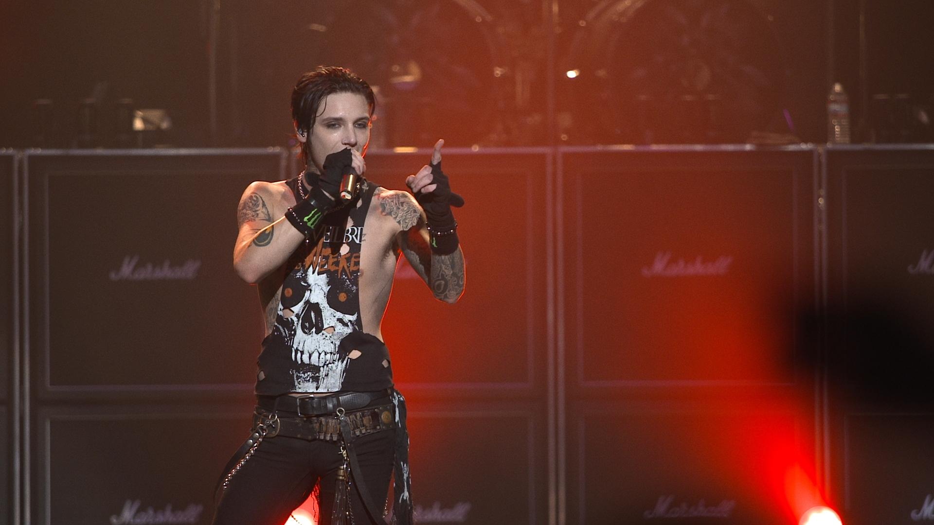 Black Veil Brides frontman performs on stage, wearing a skull-themed tank top and holding a microphone, with Marshall amplifiers in the background.