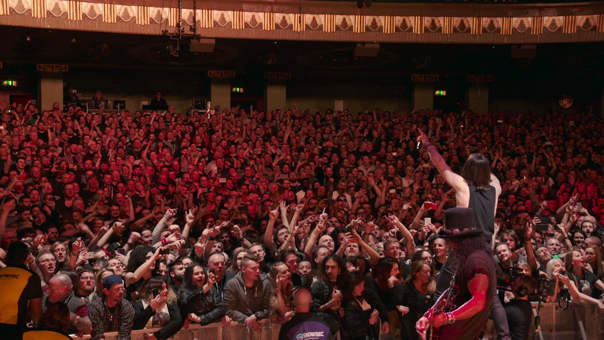 Slash featuring Myles Kennedy and the Conspirators on stage points to an enthusiastic crowd of concert-goers in a packed venue.