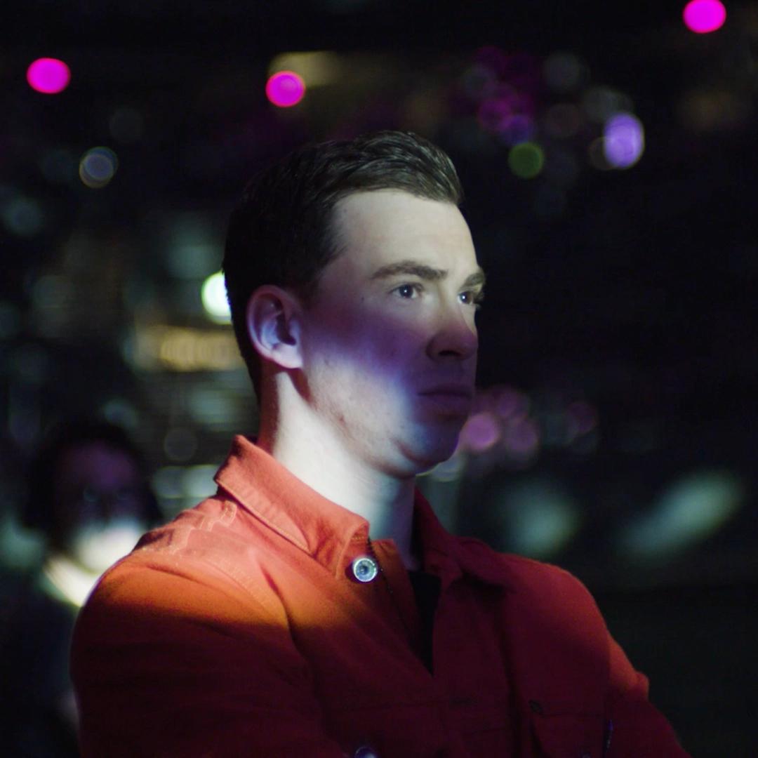 Hardwell stands in a dimly lit room with colorful lights in the background.