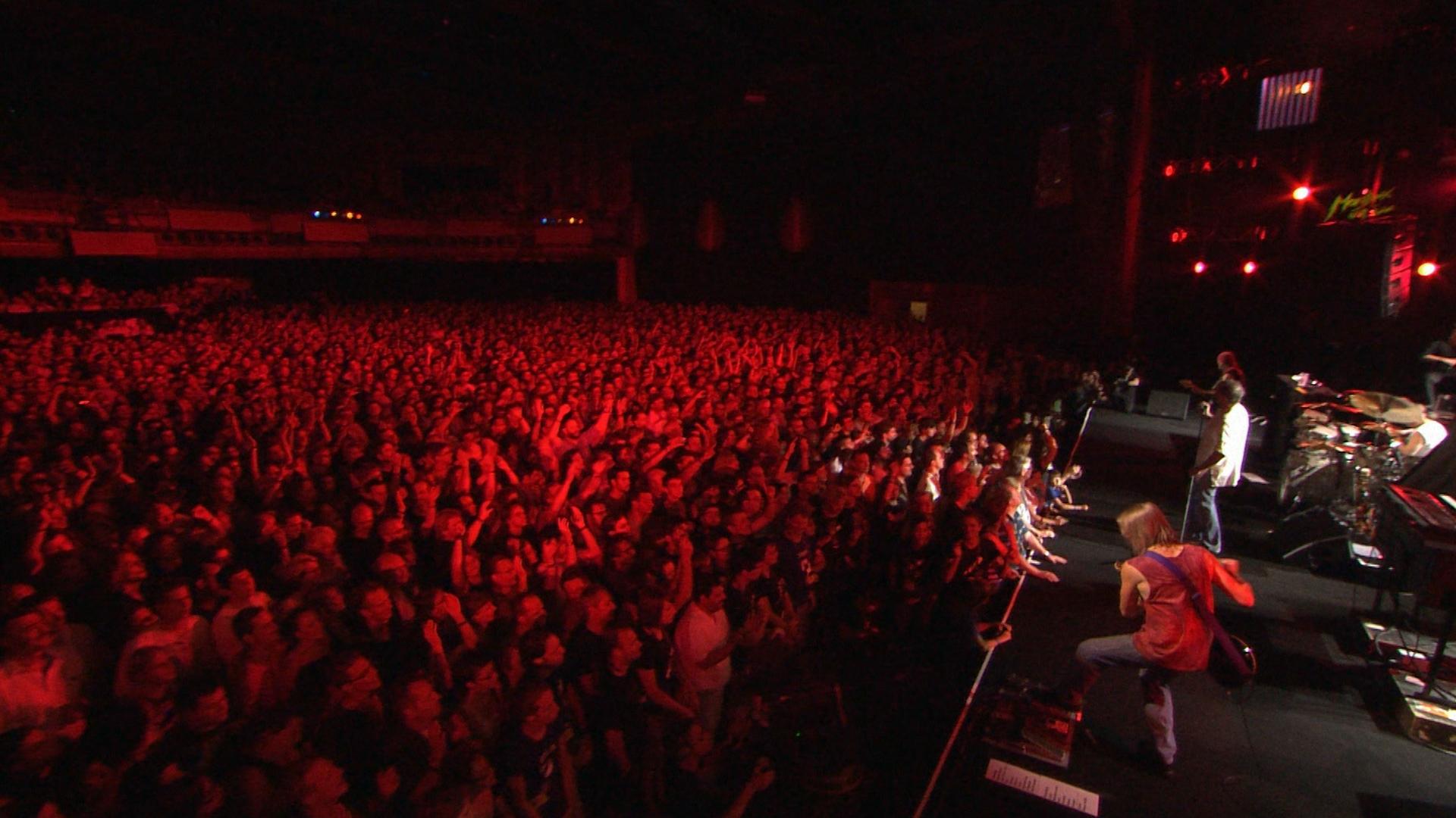 A large crowd watches deep purple perform on stage under red lighting in a dark concert venue.