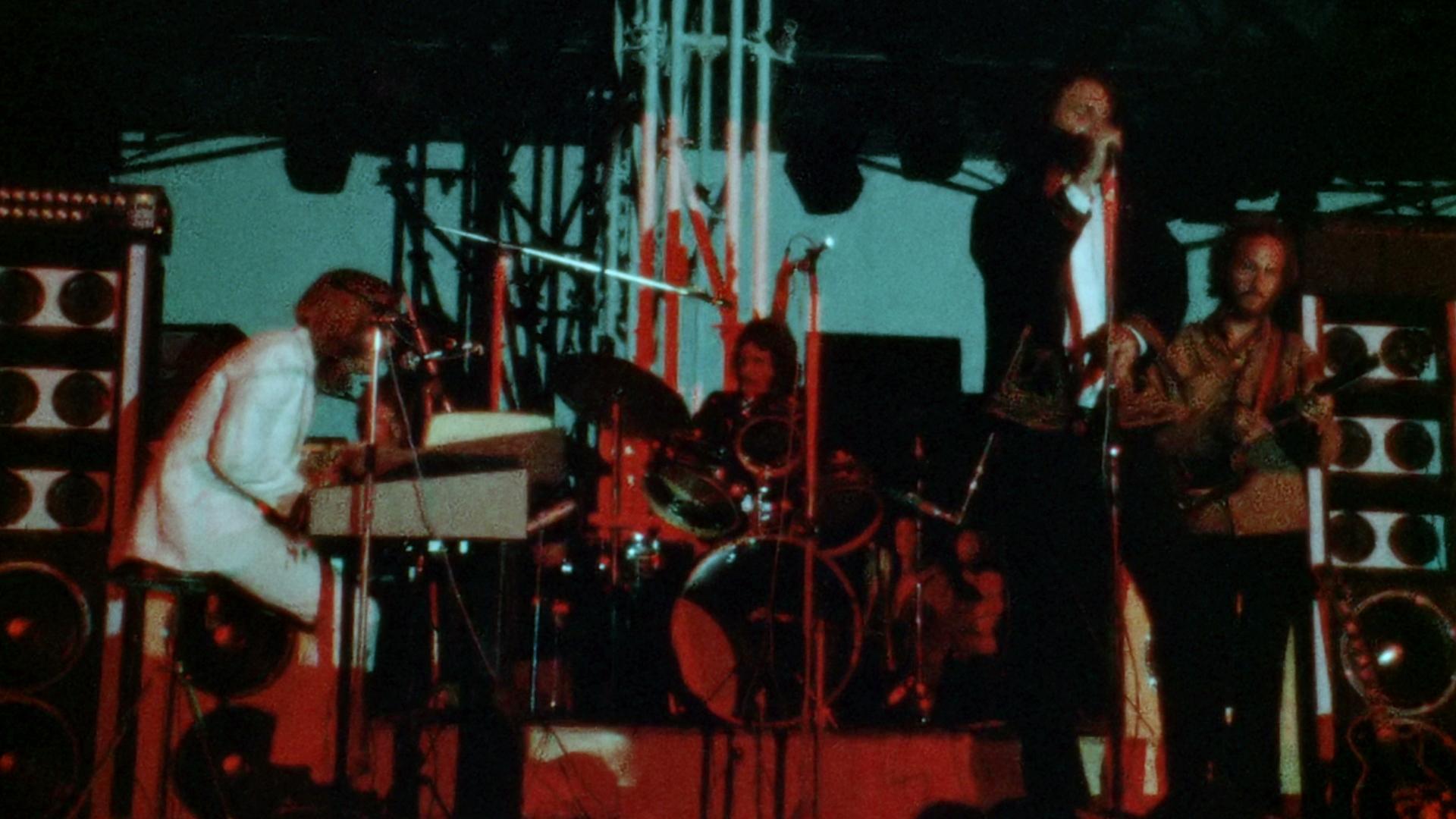 The Doors perform on stage with instruments including a keyboard, drums, and guitar, under stage lighting.