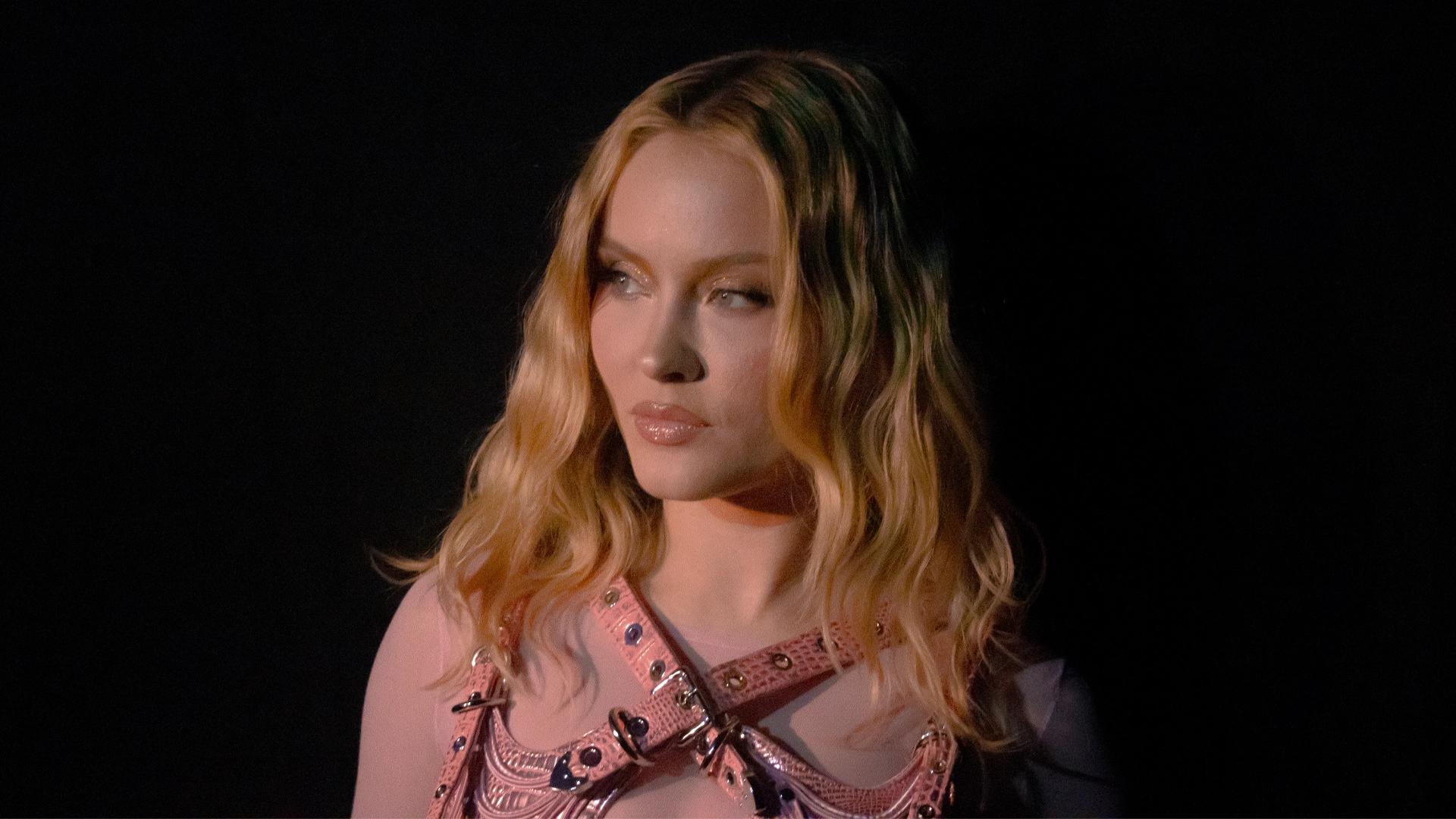 Zara Larsson in a pink outfit against a dark background.