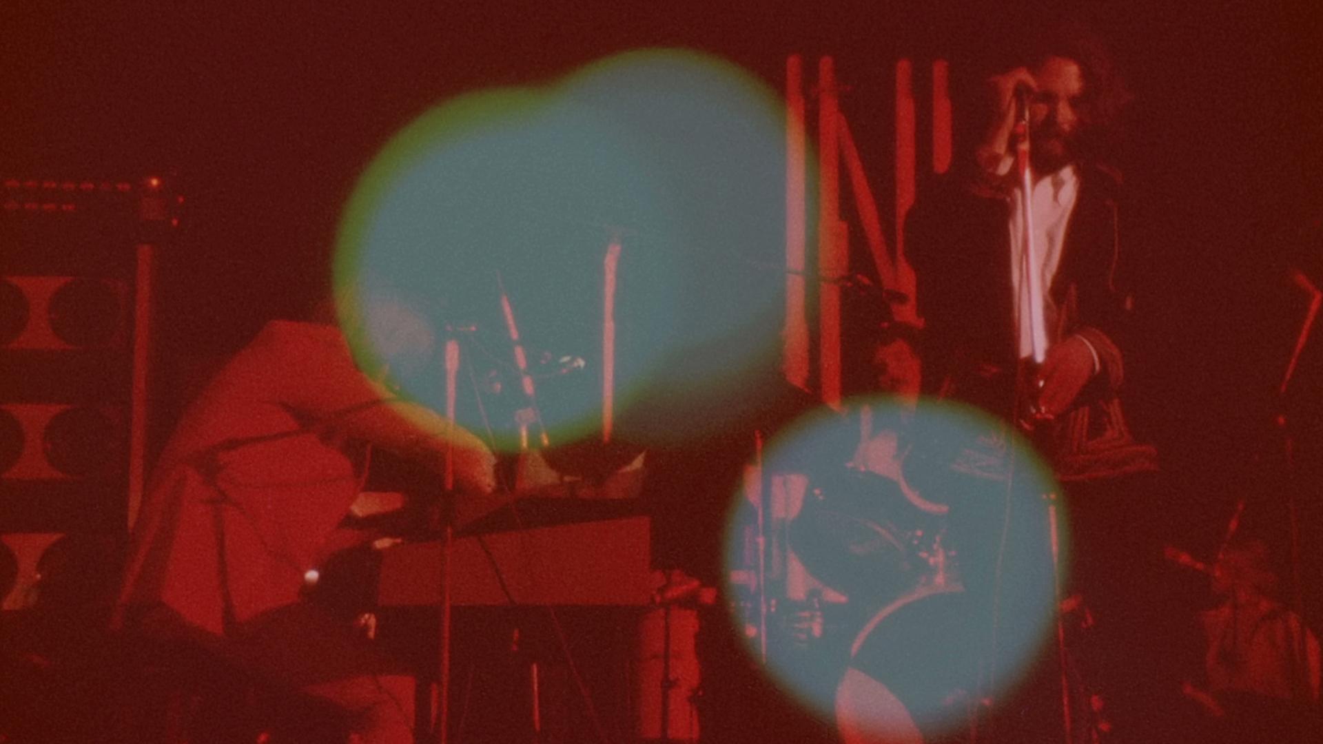 the doors perform onstage under red lighting. The image includes large green light flares, partially obscuring the band members.