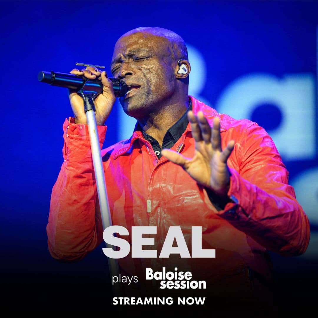 Seal sings into a microphone on stage, wearing a red jacket, with “Seal plays Baloise Session Streaming Now” text overlayed.