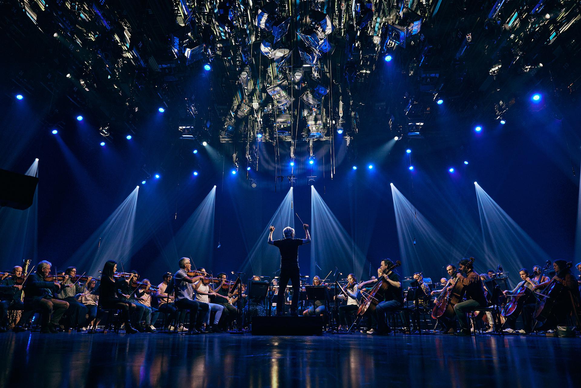 Conductor Peter Breiner leading the Royal Philharmonic Orchestra at the recording of global livestream performances of Igor Stravinsky's The Firebird, Petrushka, and The Rite Of Spring under blue lights