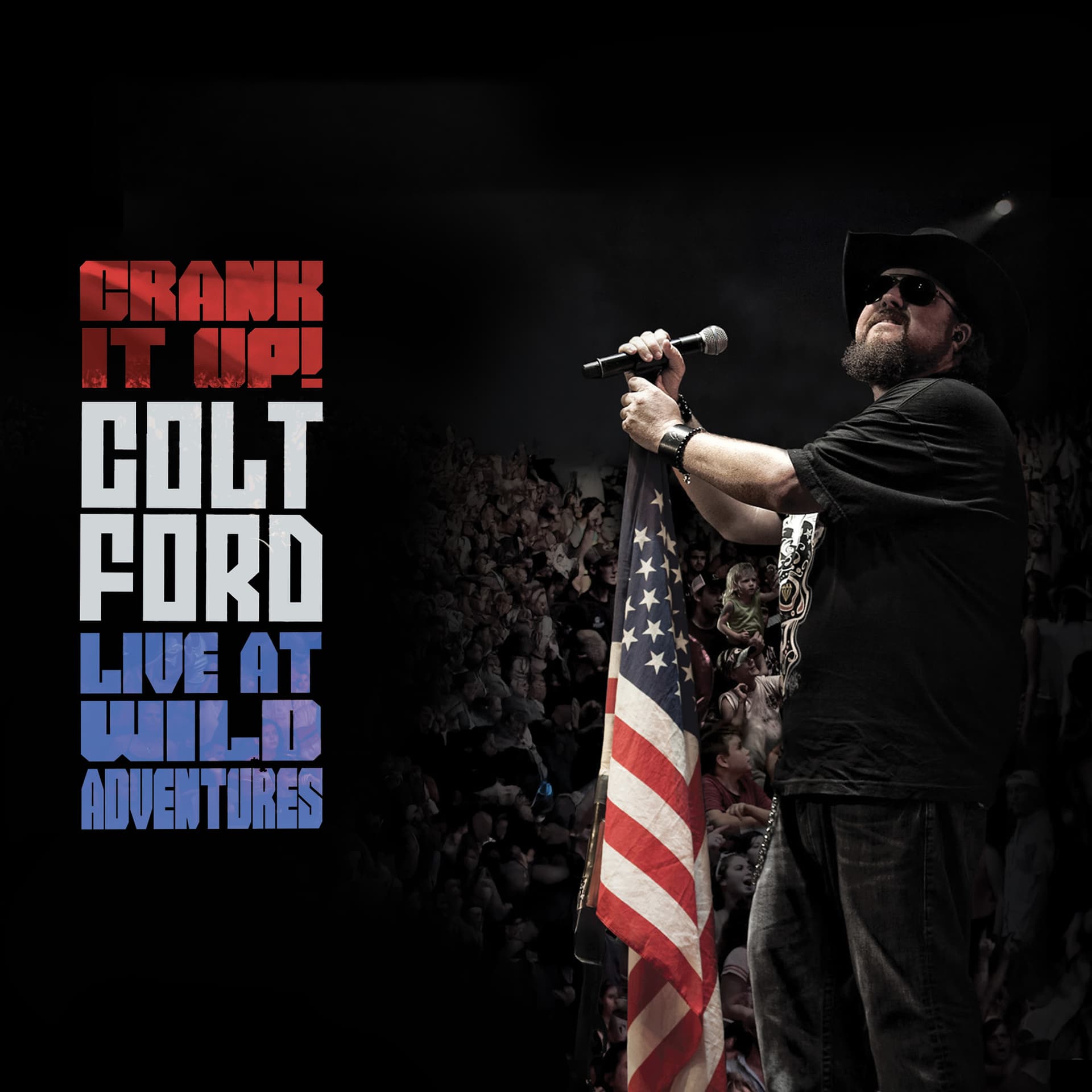 A man in sunglasses and a cowboy hat sings on stage holding a microphone and an American flag in front of a crowd. Text reads "Crank It Up! Colt Ford Live at Wild Adventures.