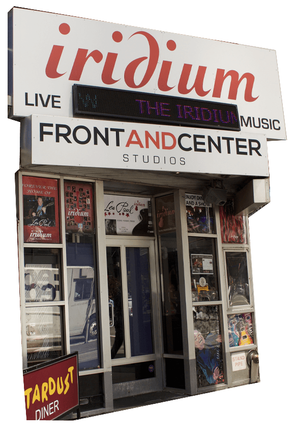 The exterior entrance of Iridium, a live music venue and studio, with posters and signs displayed on the windows and walls.