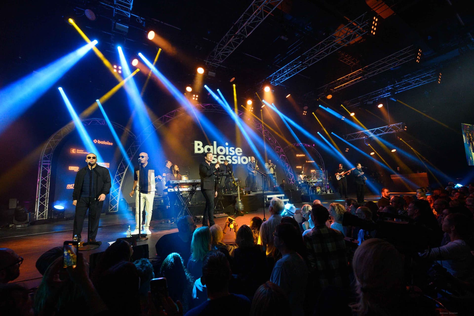 ub40 performs on stage under colorful lights at the Baloise Session music festival, with an audience watching in the foreground.
