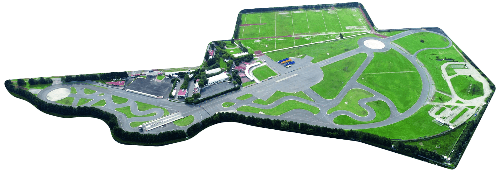 Aerial view of a large driving test or training track with various road layouts surrounded by green fields and nearby residential areas.
