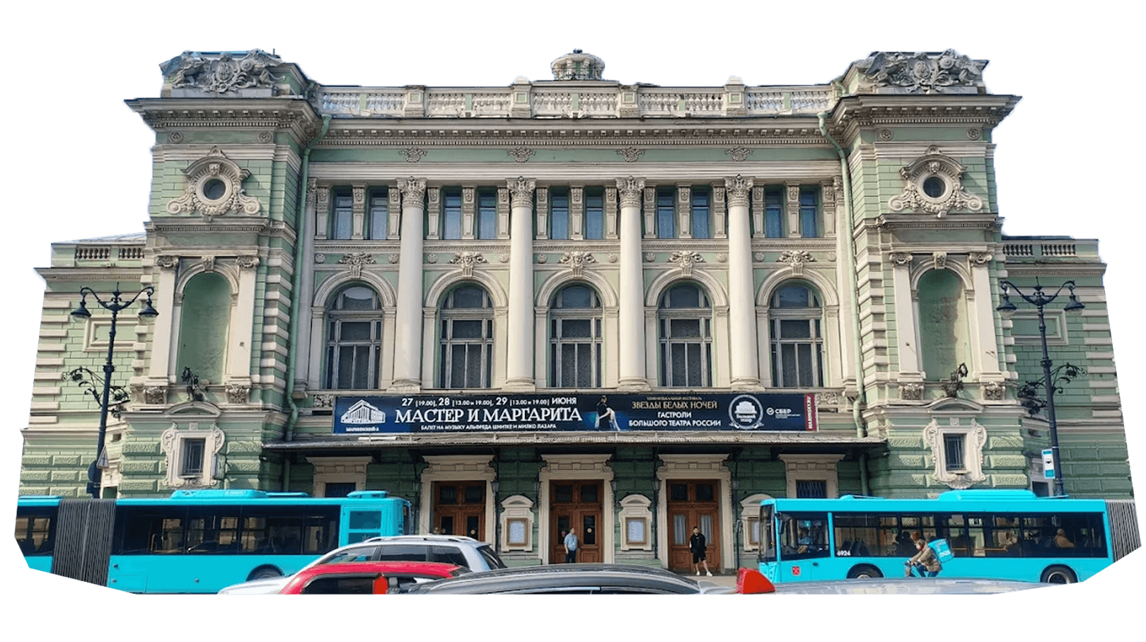 Historic theater building with ornate architecture, large columns, and decorative sculptures, with blue buses and cars parked in front. Banner above the entrance displays event information in Cyrillic script.