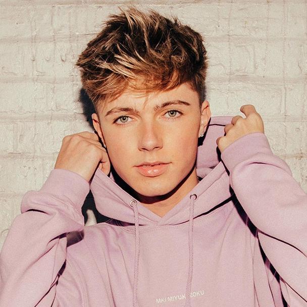 HRVY wearing a pink hoodie in front of a white brick wall