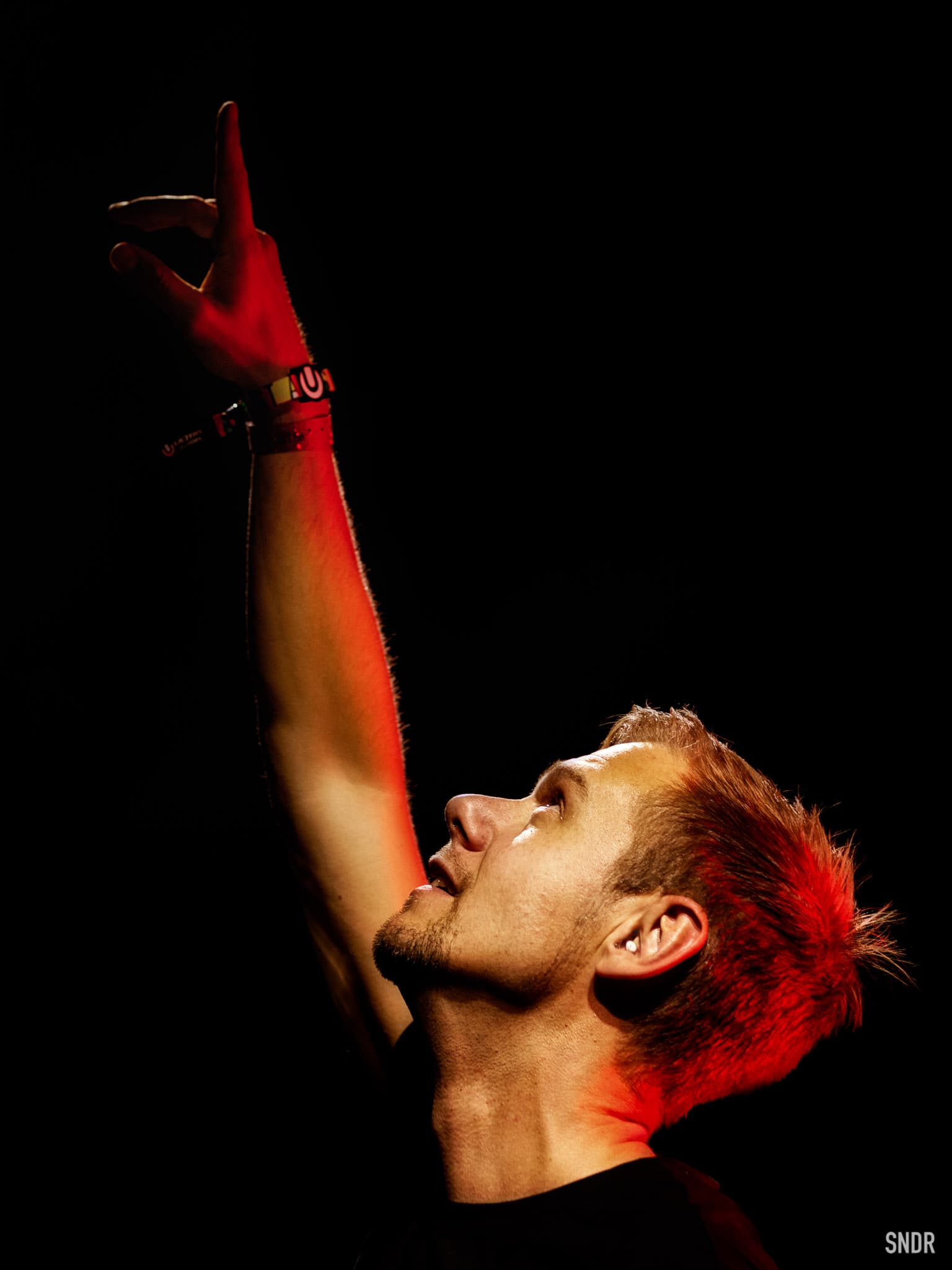 Armin Van Buuren with one hand raised above his head looking towards the heavens