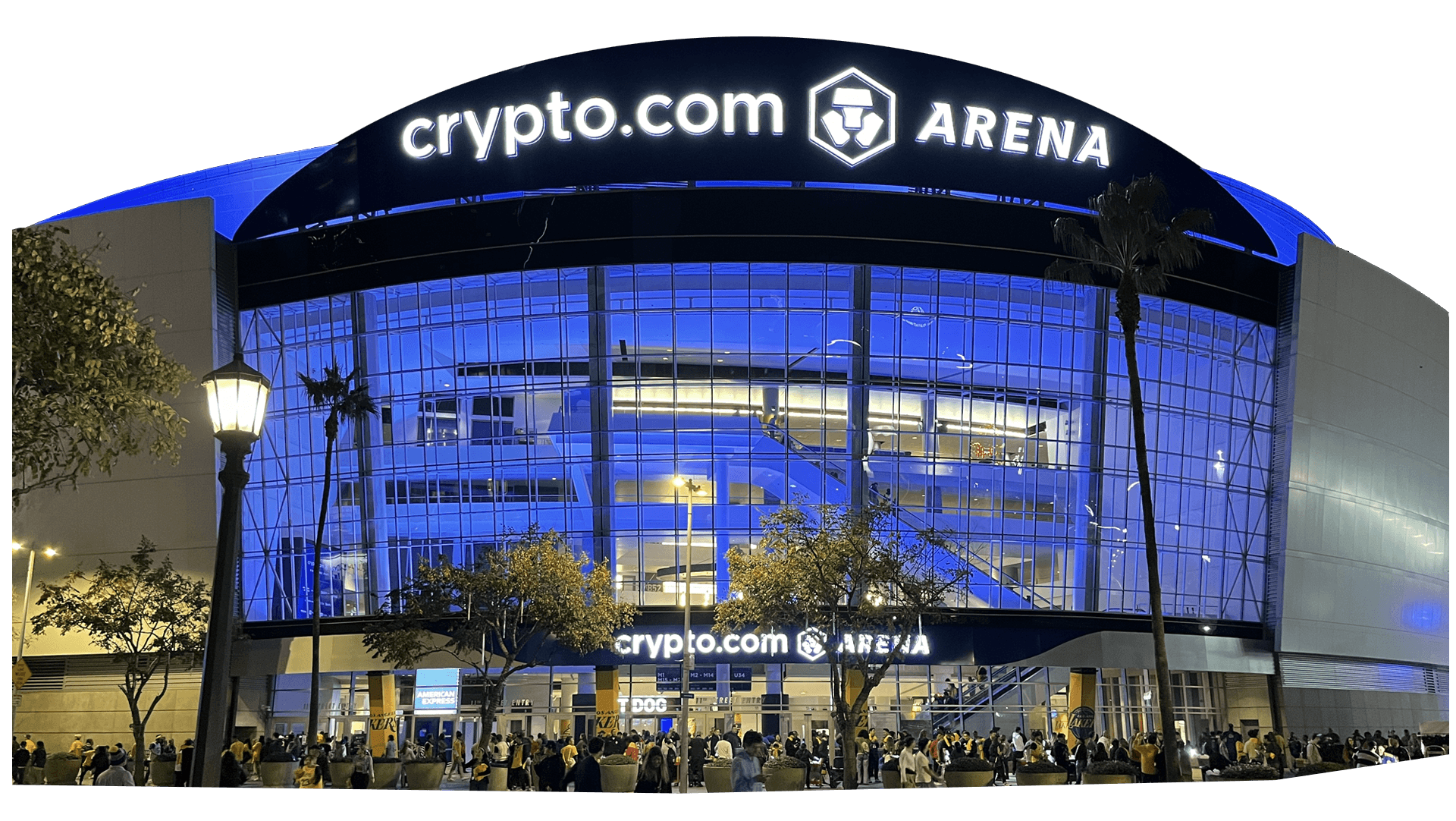 Exterior view of Crypto.com Arena at night, with large illuminated signage and crowds gathered outside the entrance.