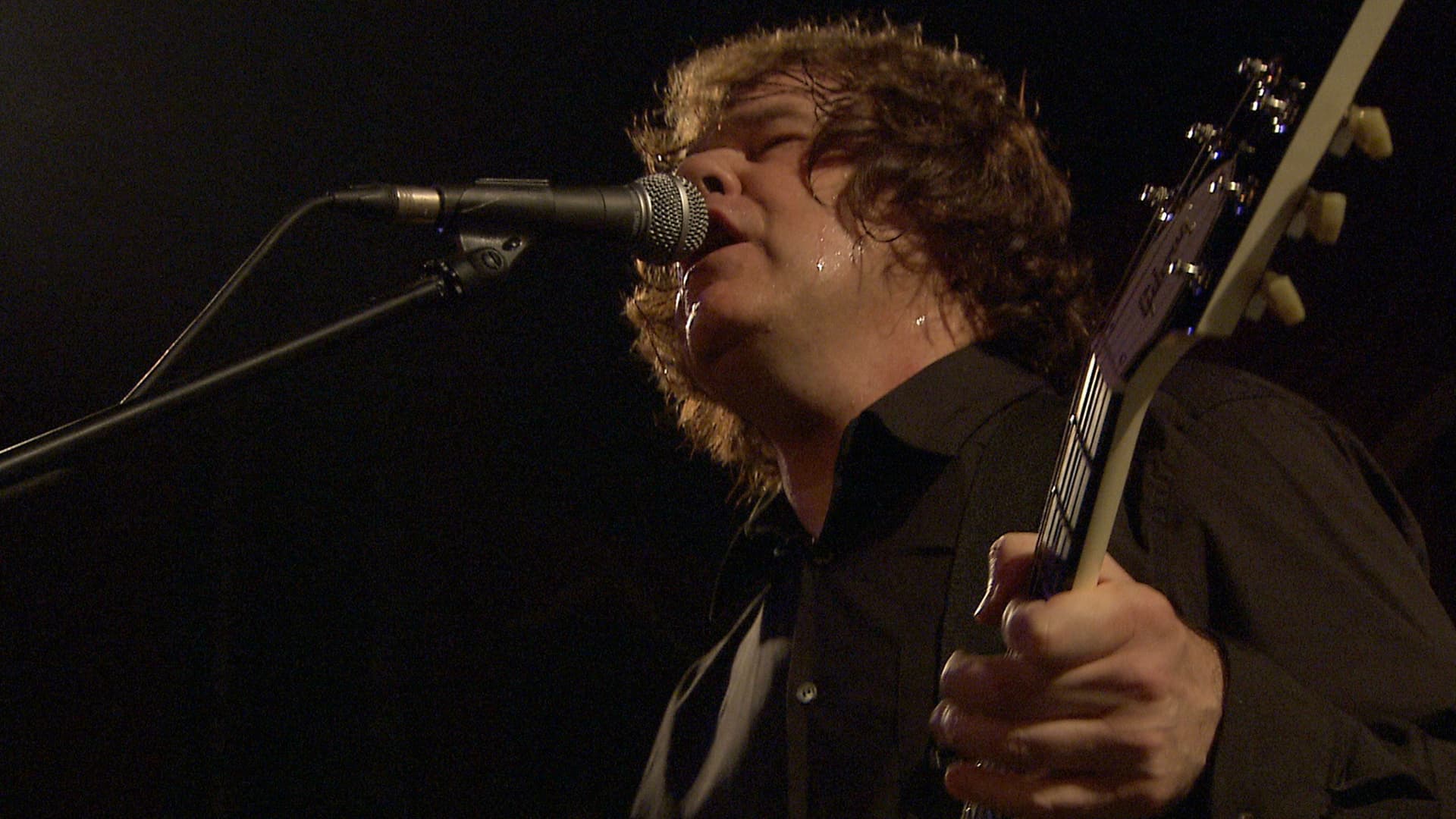 Gary Moore passionately singing into a microphone while holding a guitar on stage.