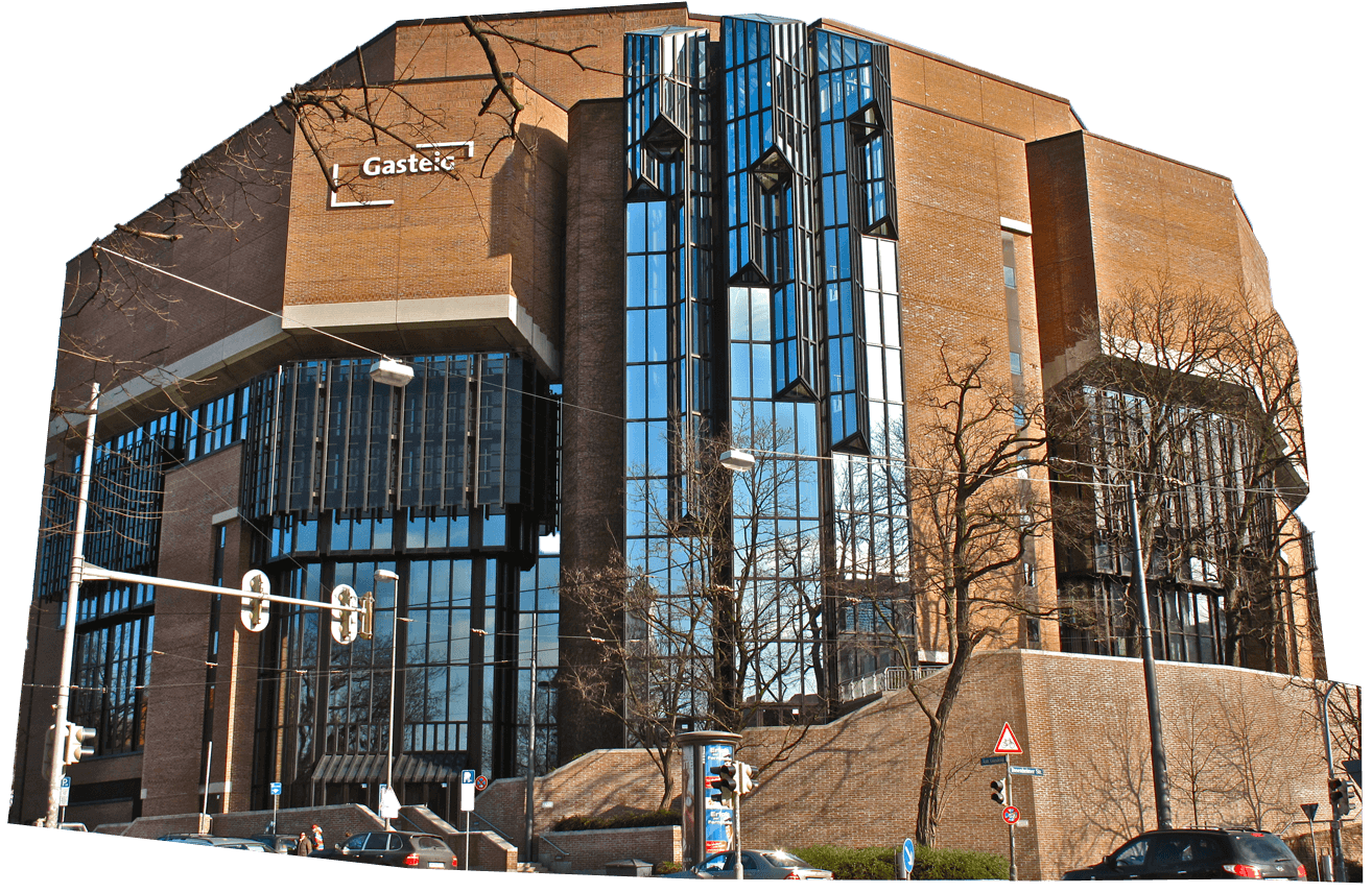 A large modern brick and glass building with angular architecture, labeled "Gasteig," stands against a clear blue sky with bare trees in front.