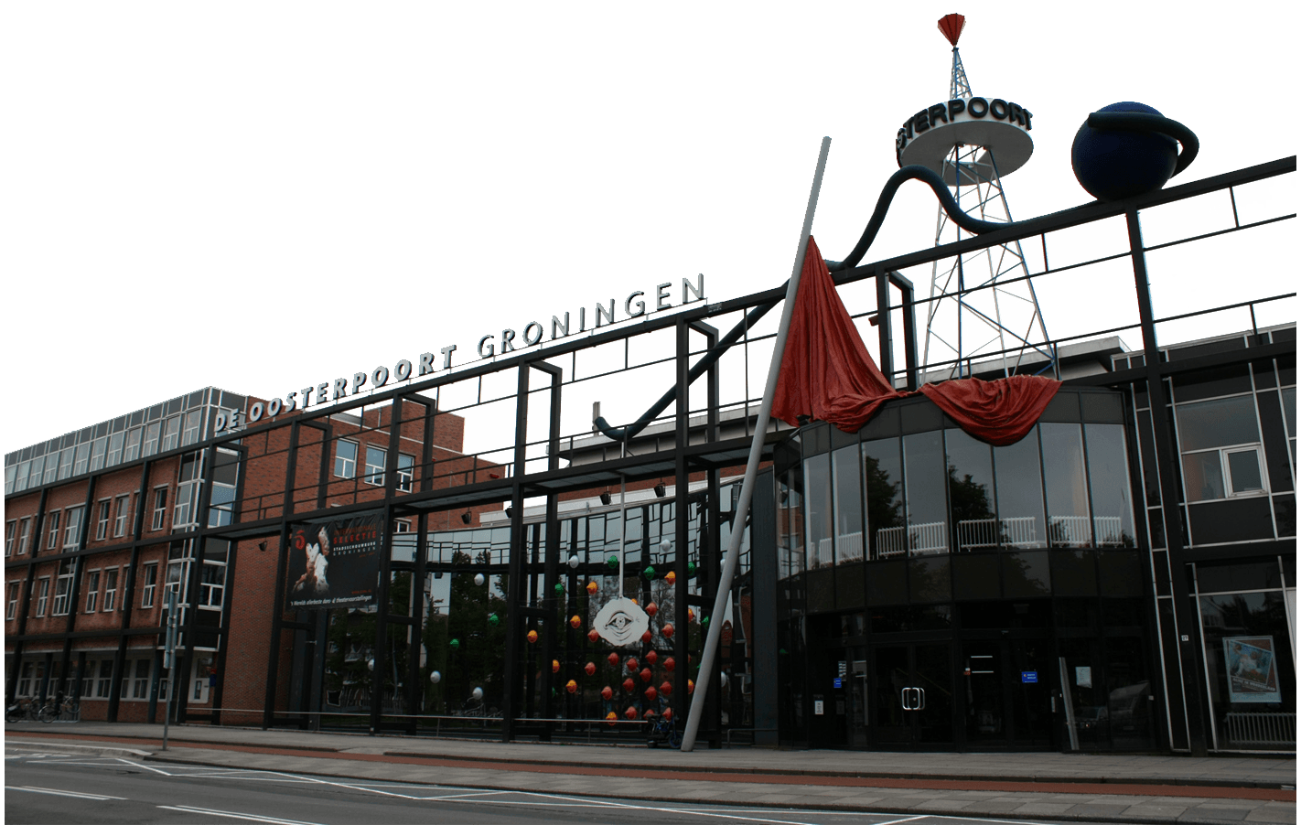 The exterior of De Oosterpoort Groningen, a modern building with large glass windows, red brick sections, and artistic metal structures above the entrance.