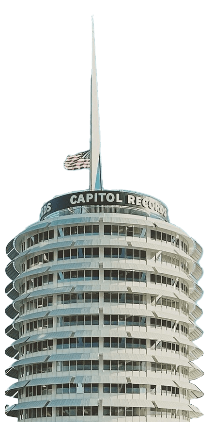 Capitol Records building with multiple windows, topped by a tall spire and an American flag, featuring the signage "Capitol Records" on a clear day.
