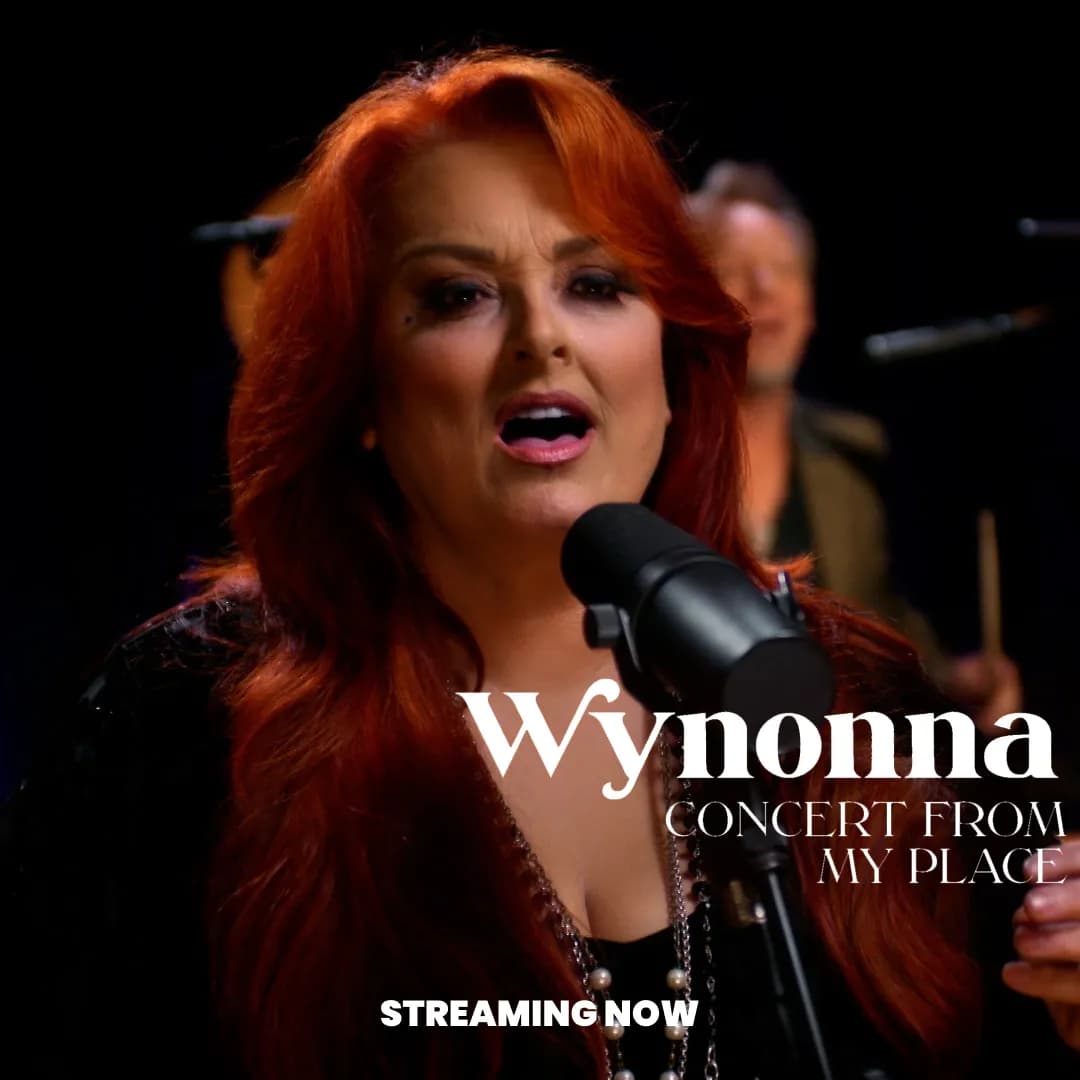 Wynonna Judd with long red hair sings into a microphone. Text reads: "Wynonna Concert From My Place. Streaming Now.