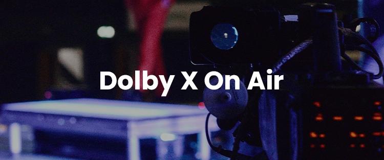 A camera focused on the text "dolby x on air" glowing in white against a blurred background of broadcasting equipment.
