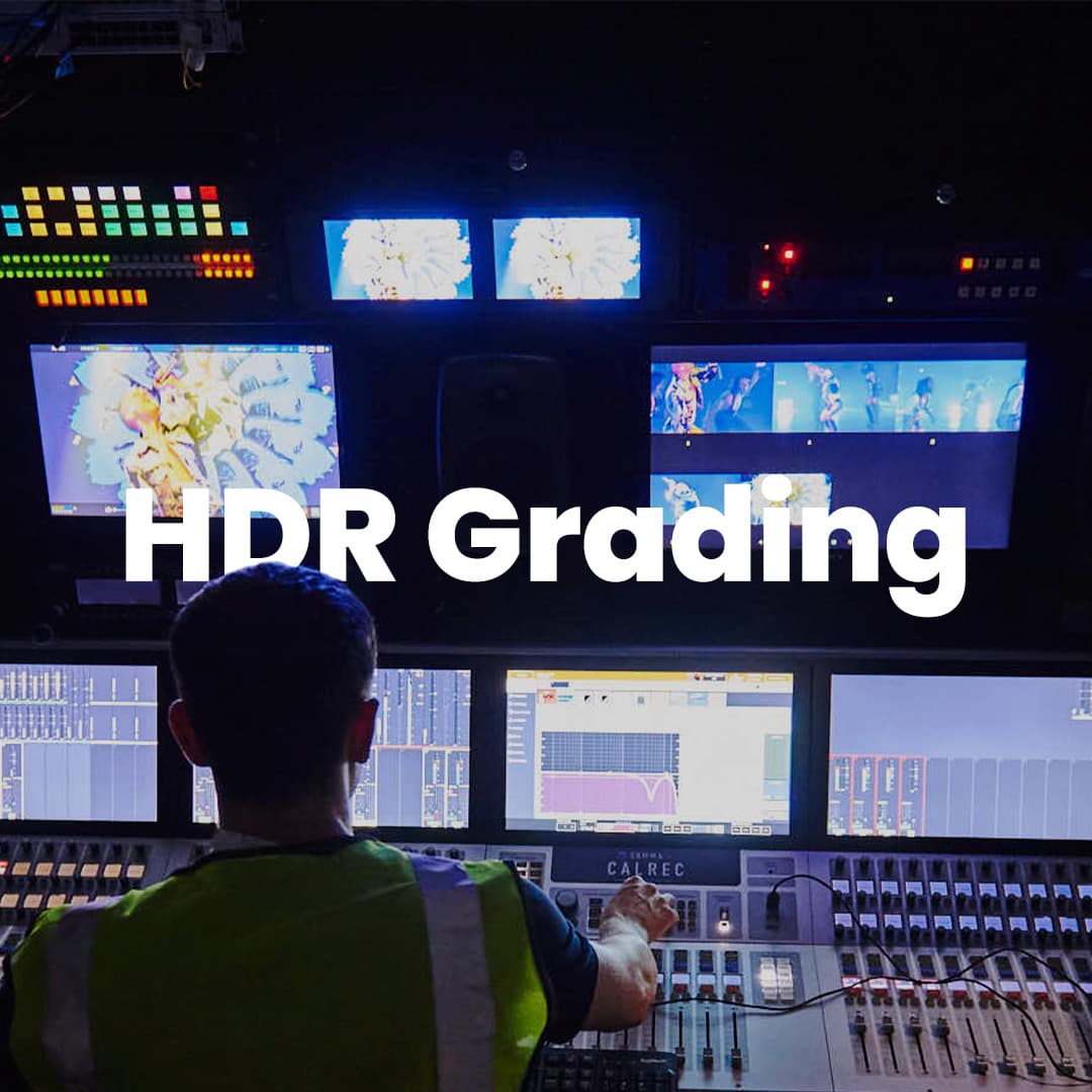 A person in a green vest works at a control panel with multiple screens displaying video content, labeled "HDR Grading.