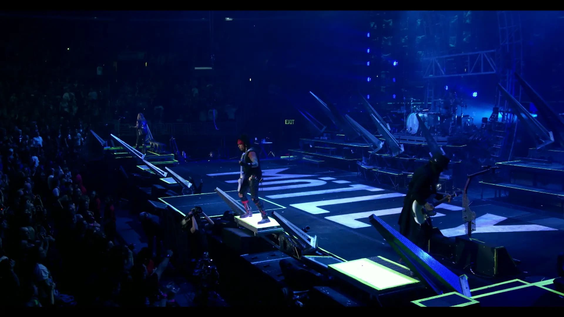 Concert scene with Motley Crue performing on a large stage, blue lighting, and an audience.