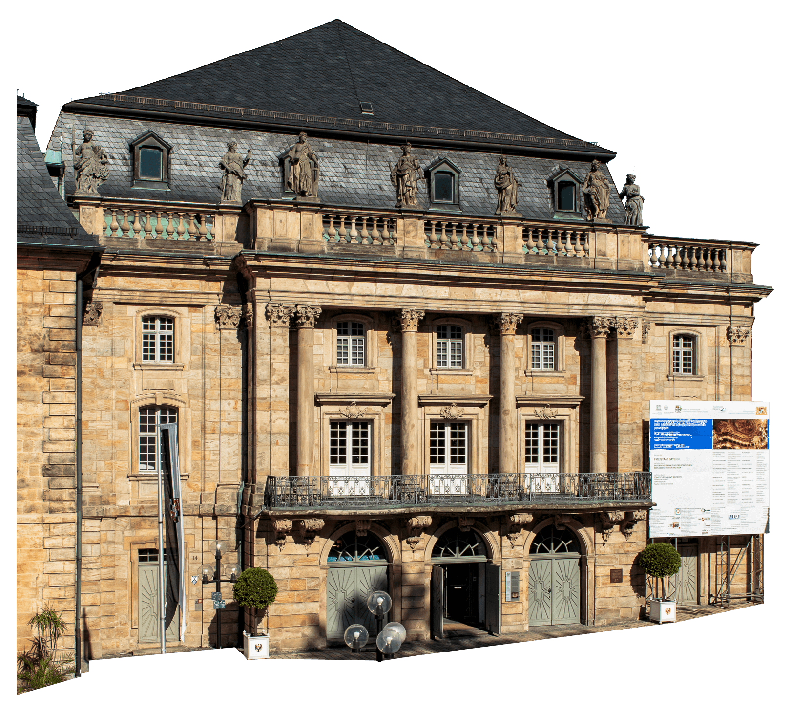 Historic stone building with columns, statues on the roofline, arched doorways, and large informational sign on the right side; clear sky overhead.