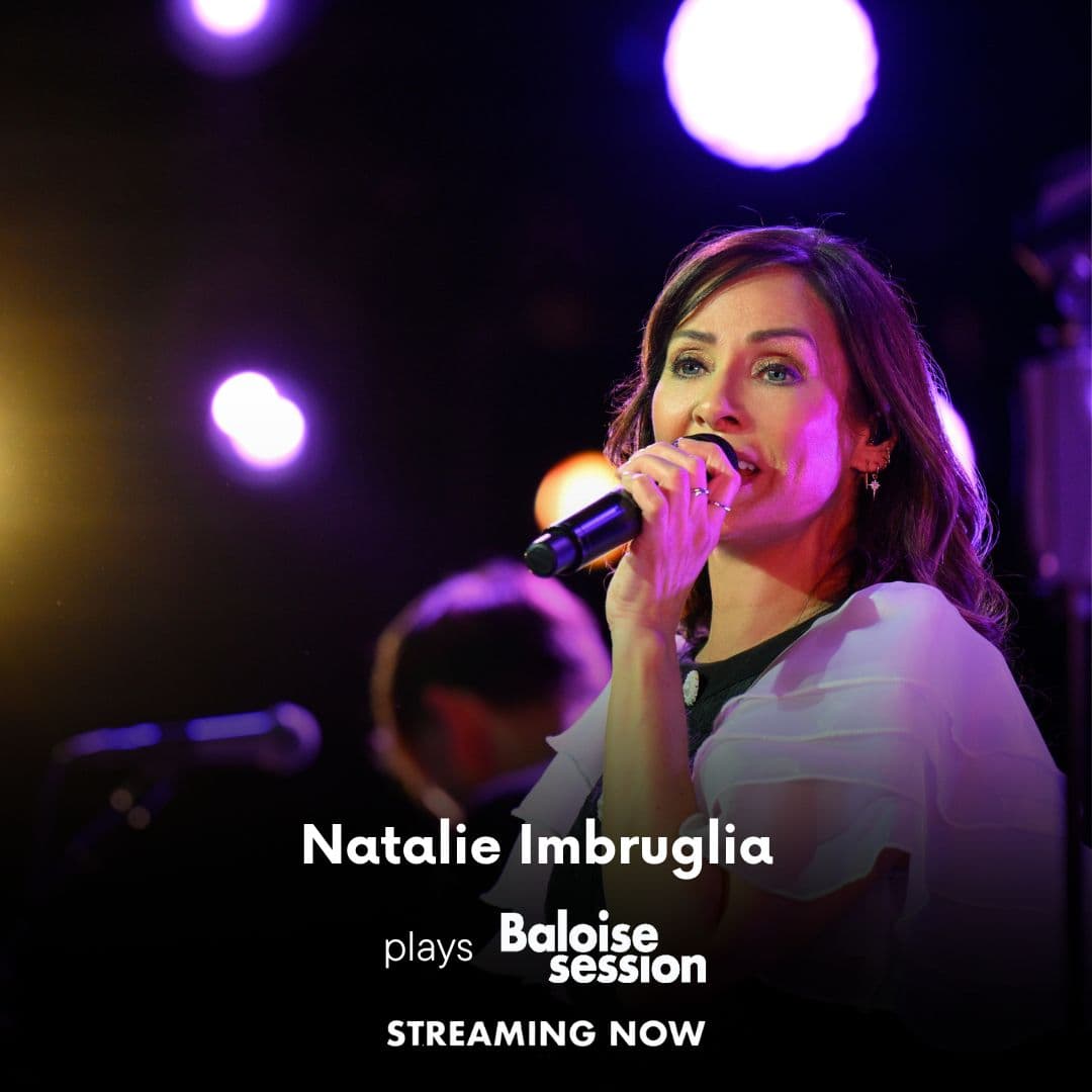 natalie imbruglia sings into a microphone on stage with colorful lights in the background. Text on image reads: "Natalie Imbruglia plays Baloise Session. Streaming now.
